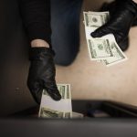 Gloved hands stealing cash from an unsecured safe